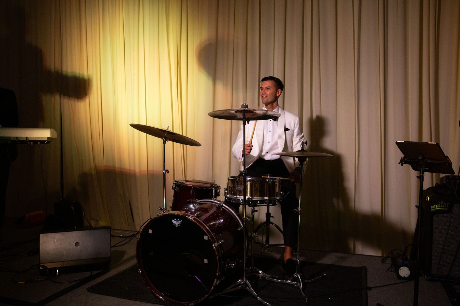 Drummer performing at wedding reception under dramatic spotlight.