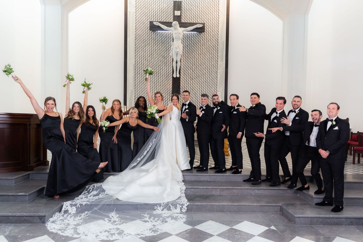 Wedding party lined up against white wall in formal black attire.