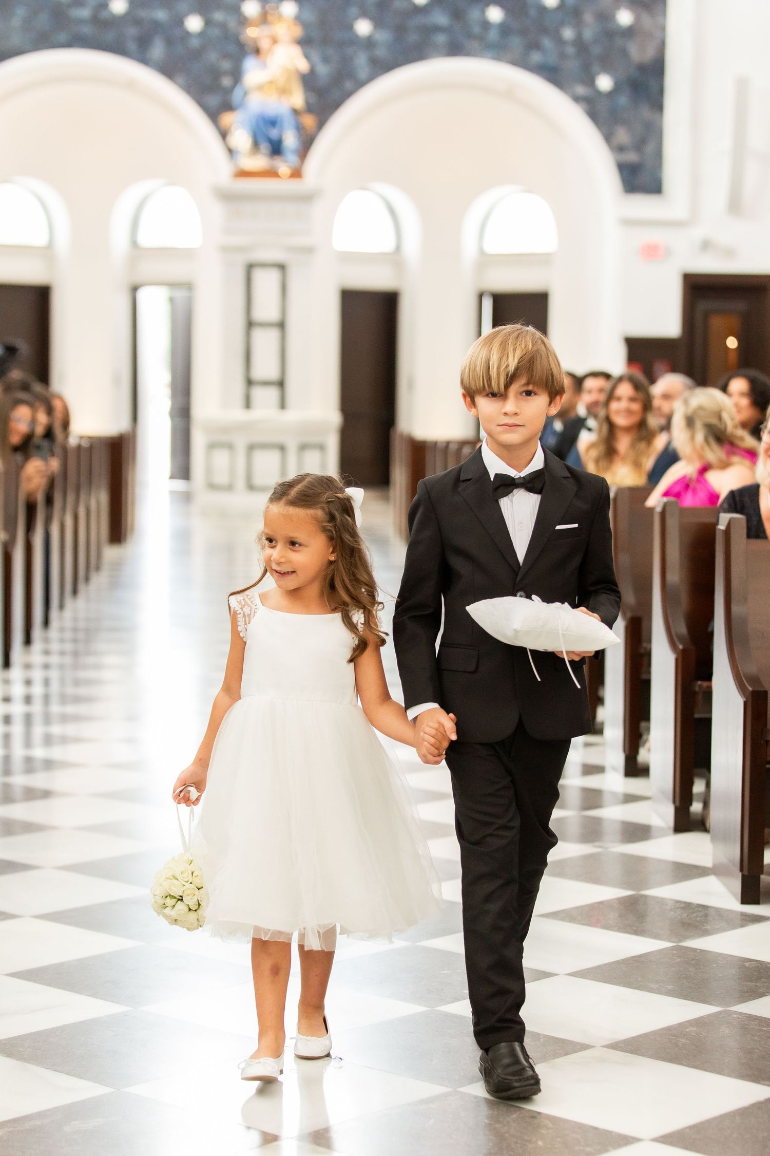 Children in white attire walking down a church aisle during a wedding ceremony.