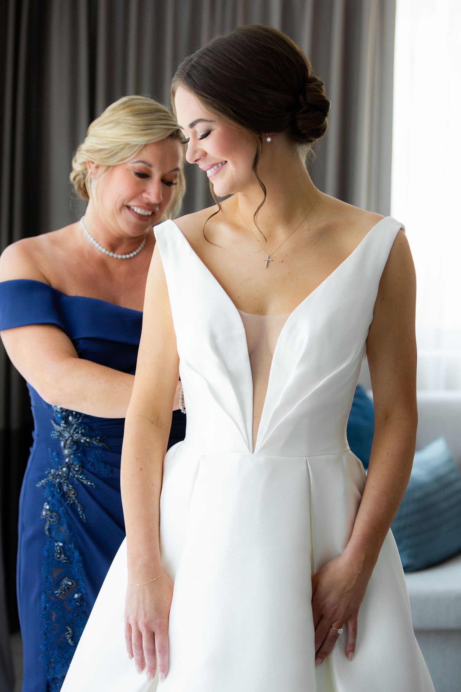 Wedding dress fitting moment with bridesmaid in navy blue gown.