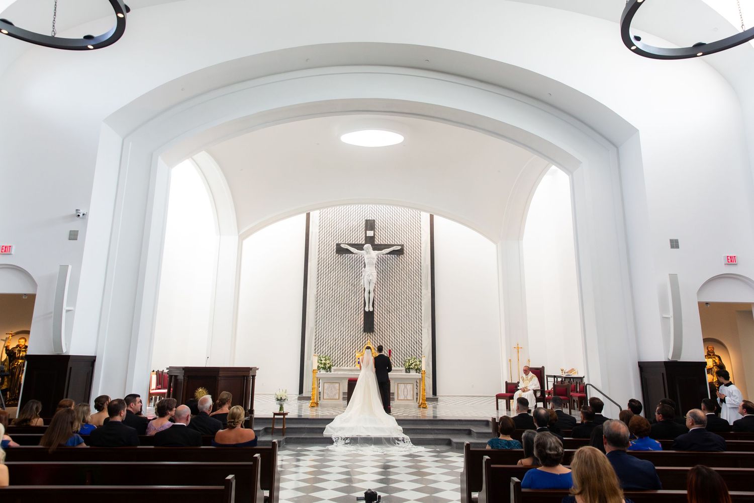 Wide angle view of church sanctuary with white arched ceilings during wedding ceremony.
