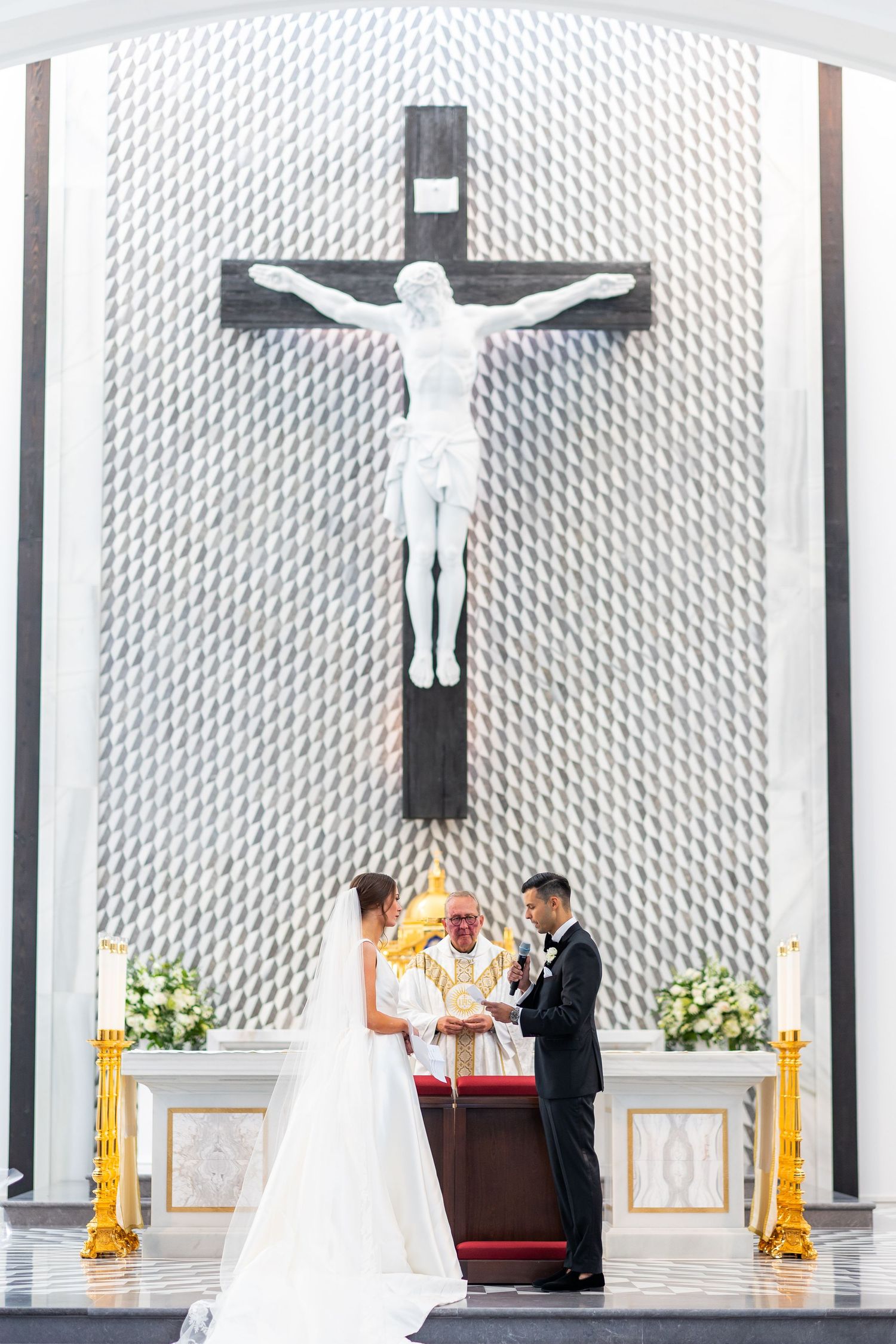 Church altar features large crucifixes against geometric patterned wall during wedding ceremony.