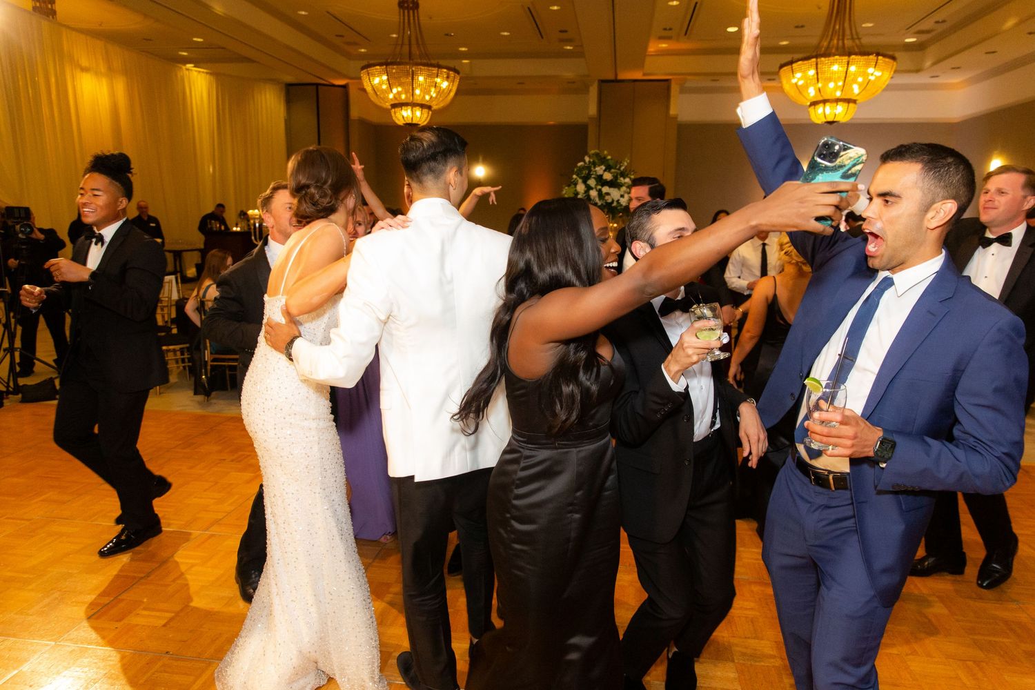 Wedding celebration with guests dancing and mingling in an elegant ballroom setting.