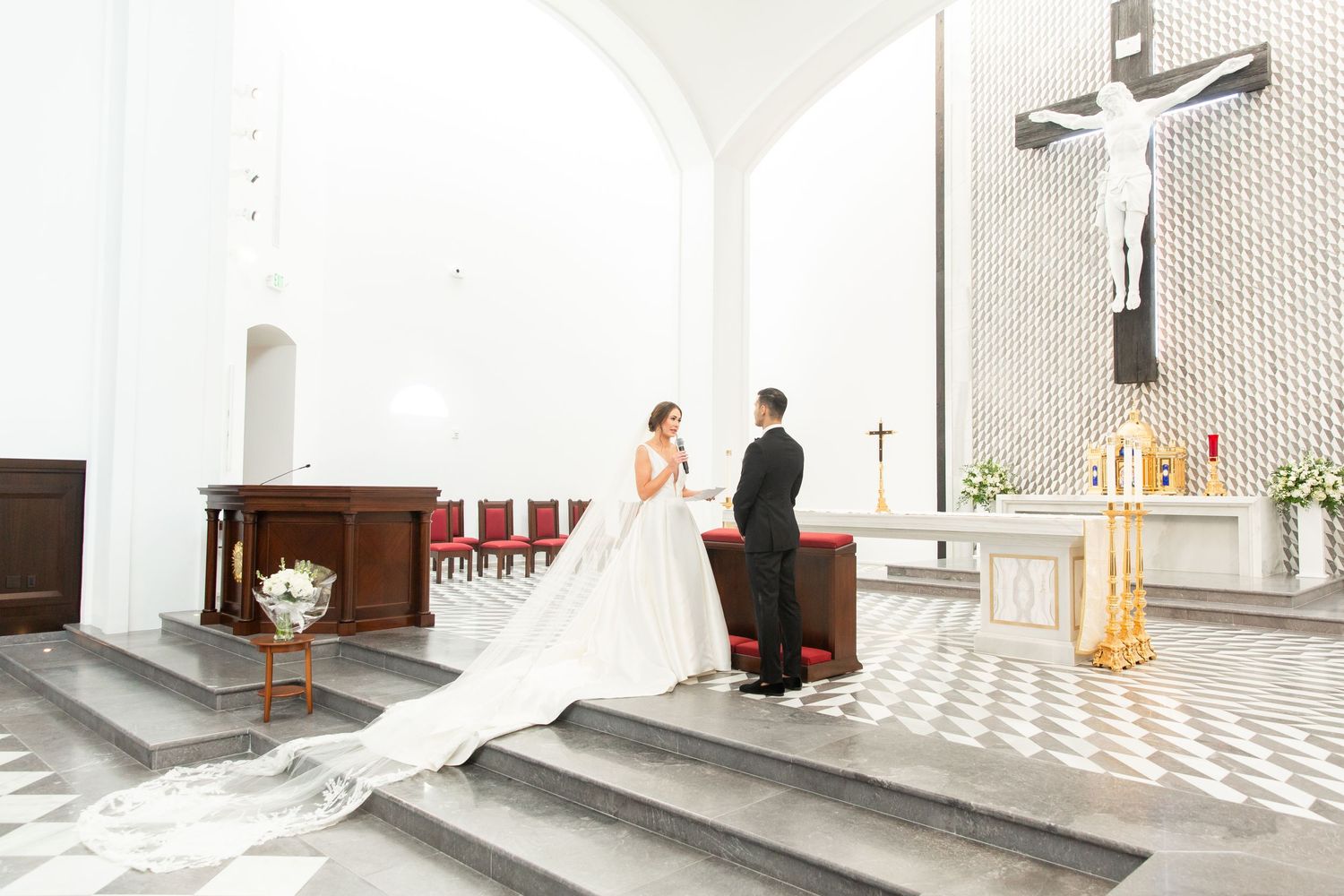 A wedding couple stands together in a modern white church with geometric wall patterns.