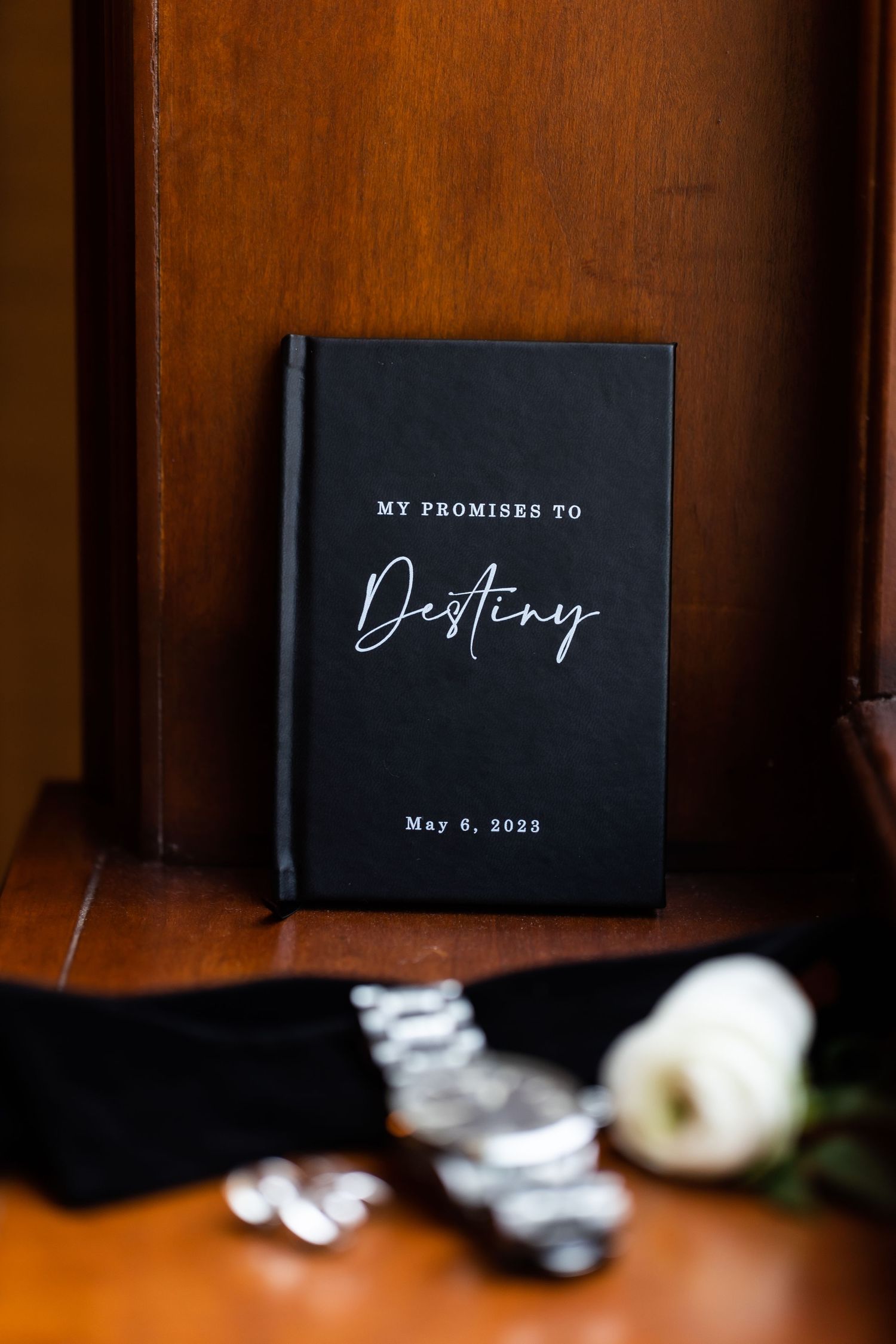 Black wedding vow book with custom lettering and date displayed on wooden surface.