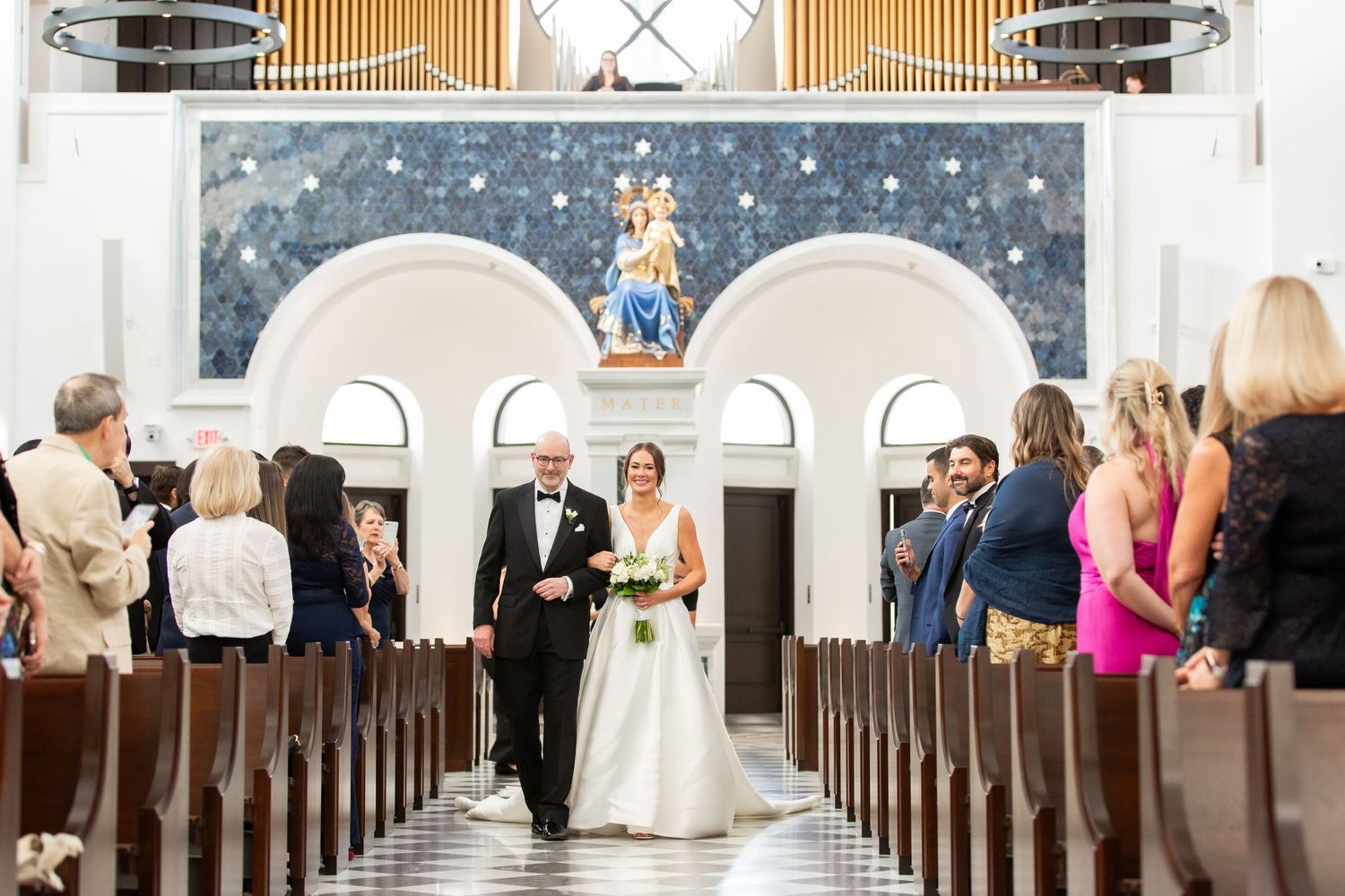 Traditional church wedding ceremony with guests seated in wooden pews along a black and white checkered aisle.