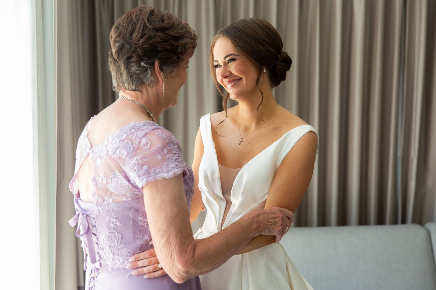 Emotional embrace between bride and family member in lavender dress.