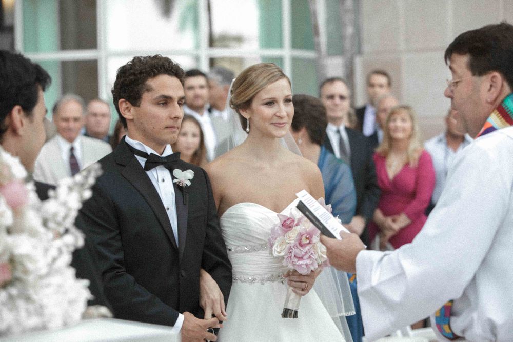 A formal wedding ceremony takes place outdoors with the couple and officiant gathered at the altar.