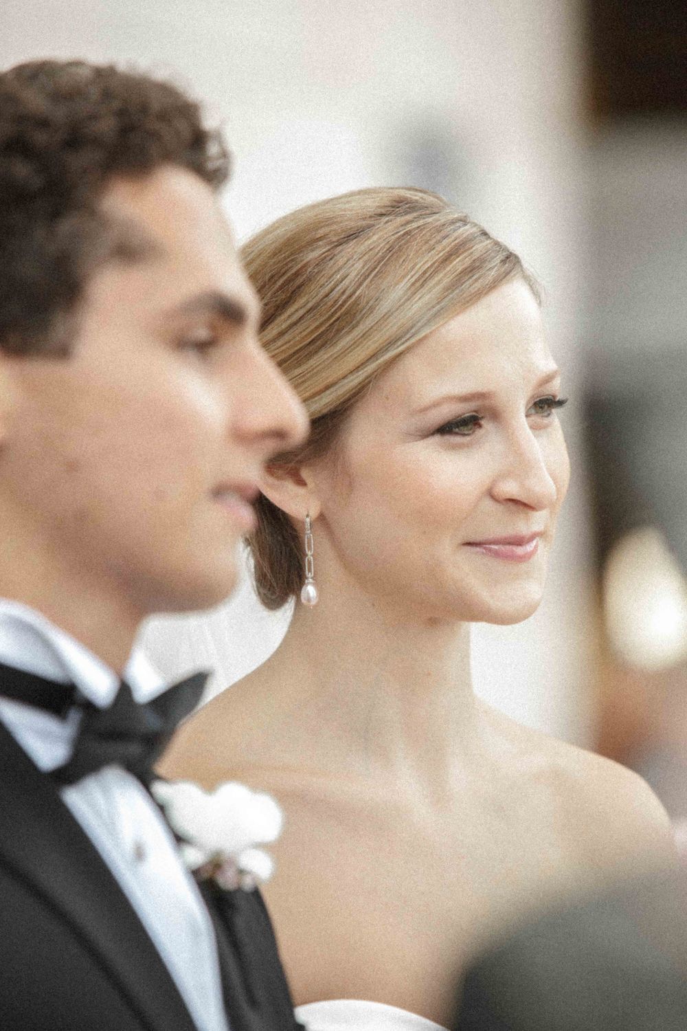 Close-up wedding portrait of a smiling couple in formal attire, with the bride in white and groom in tuxedo and bowtie.