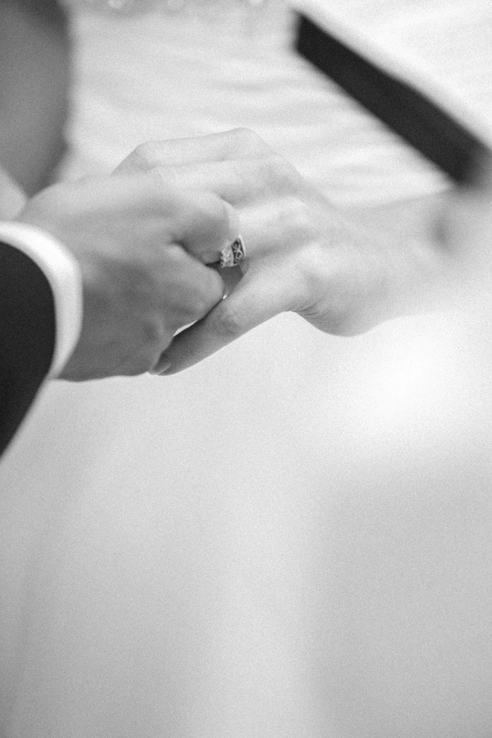 A close-up black and white photograph of hands exchanging wedding rings during a marriage ceremony.