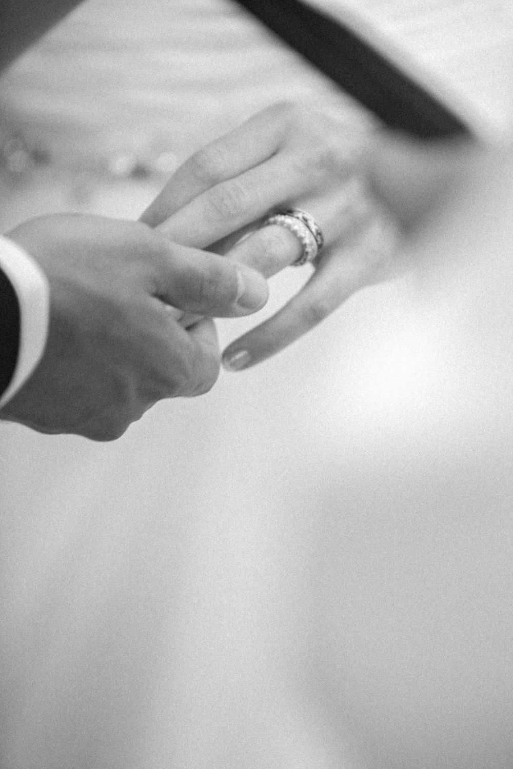 Close-up black and white photo of hands exchanging wedding rings during a marriage ceremony.