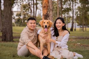 A couple sit on the ground with their Goldendoodle dog in between them