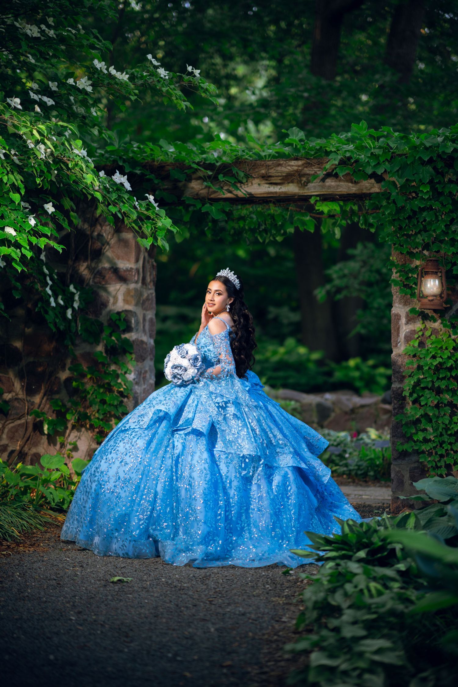 Enchanting garden photoshoot featuring flowing blue princess gown among green foliage.