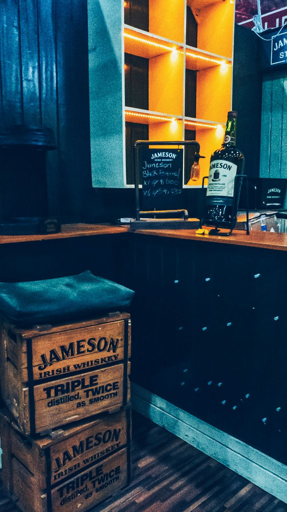 Vintage-style bar setting with stacked Jameson whiskey crates and orange neon lighting.