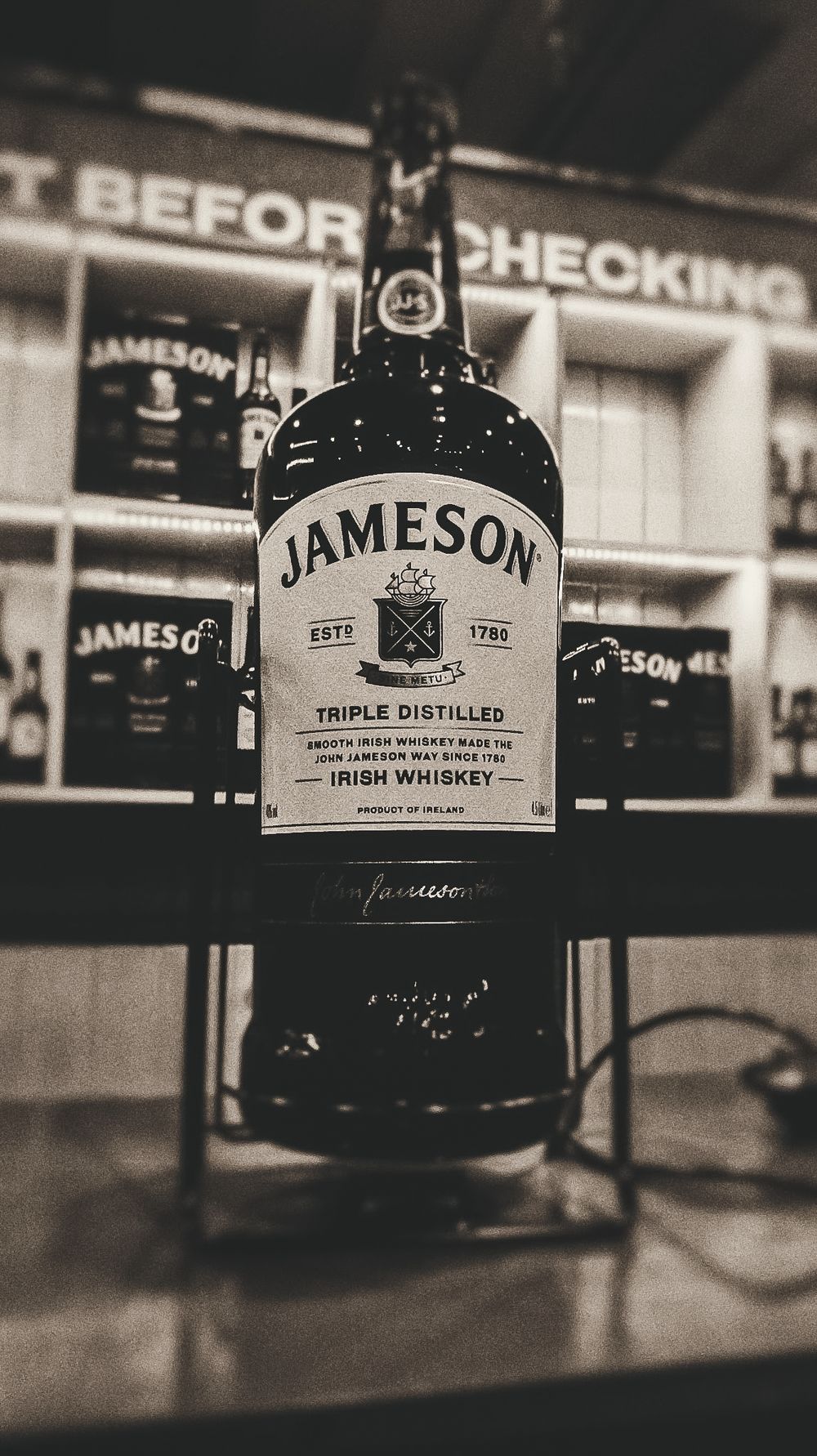 A black and white photograph of a Jameson Irish Whiskey bottle on display with other bottles in the background.