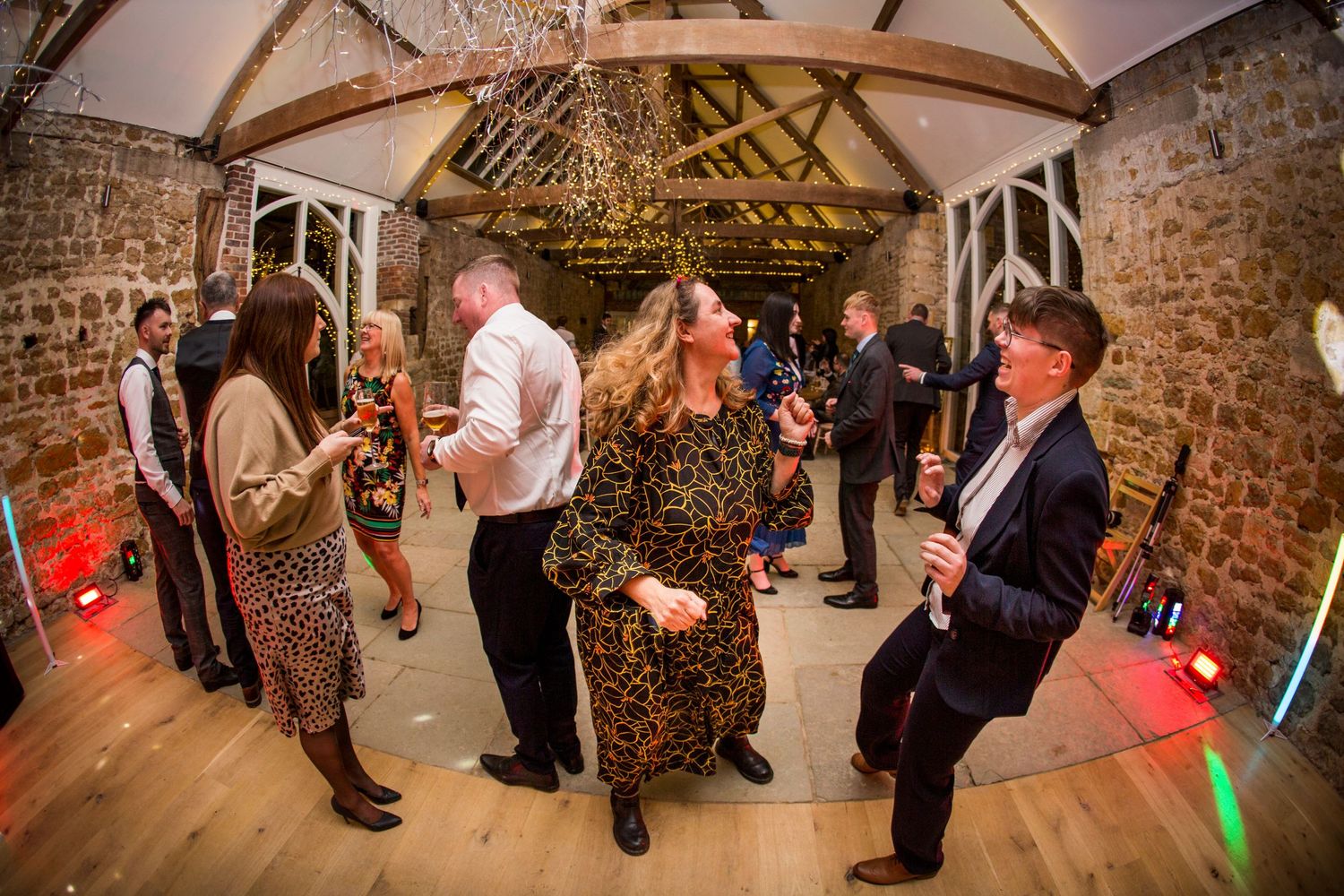 Guests dancing at a rustic barn wedding reception with stone walls and wooden beams.