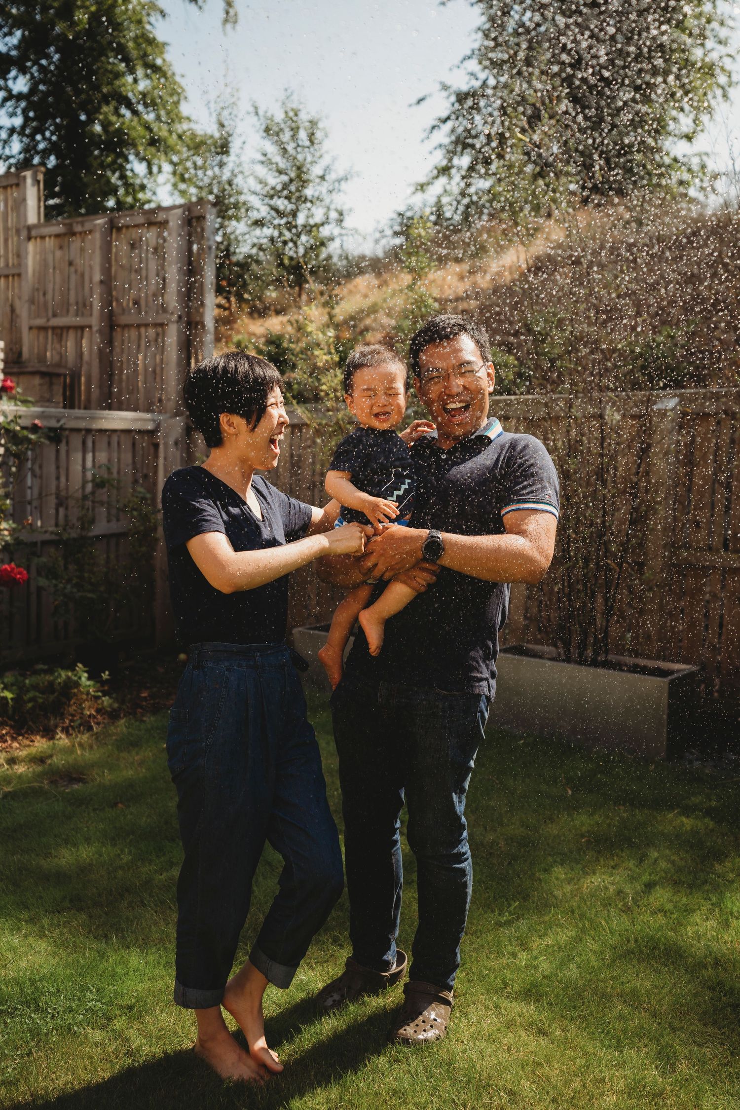 A sunny backyard family moment with water droplets sparkling in the air.