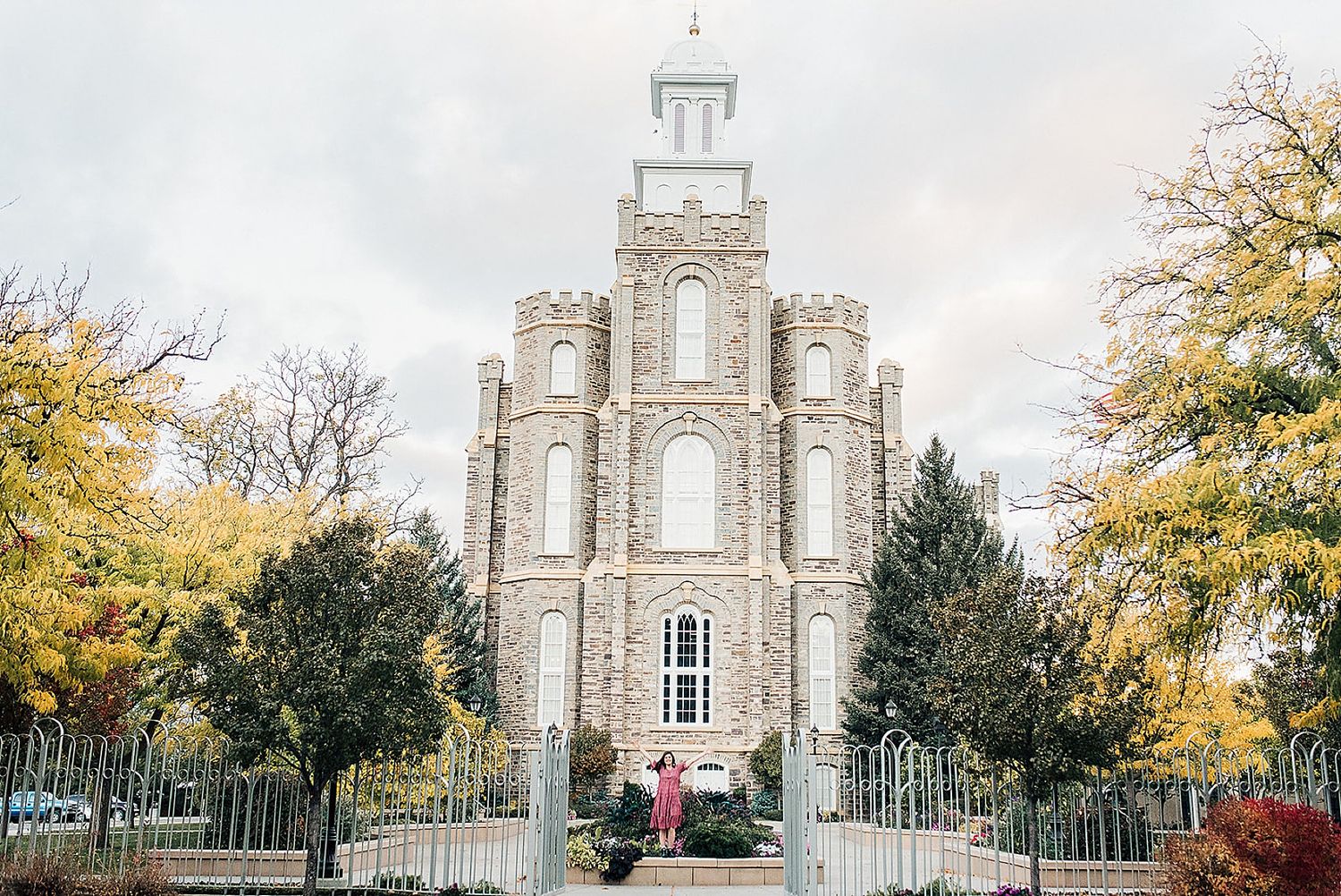 A majestic stone temple with a white spire stands against an autumn sky with colorful fall foliage.
