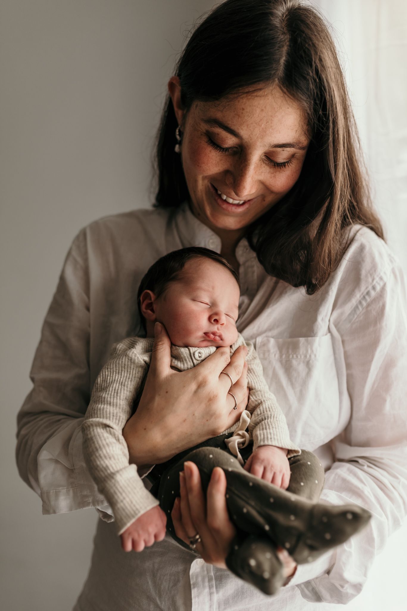 Joyful moment with sleeping newborn baby wearing cream colored outfit.