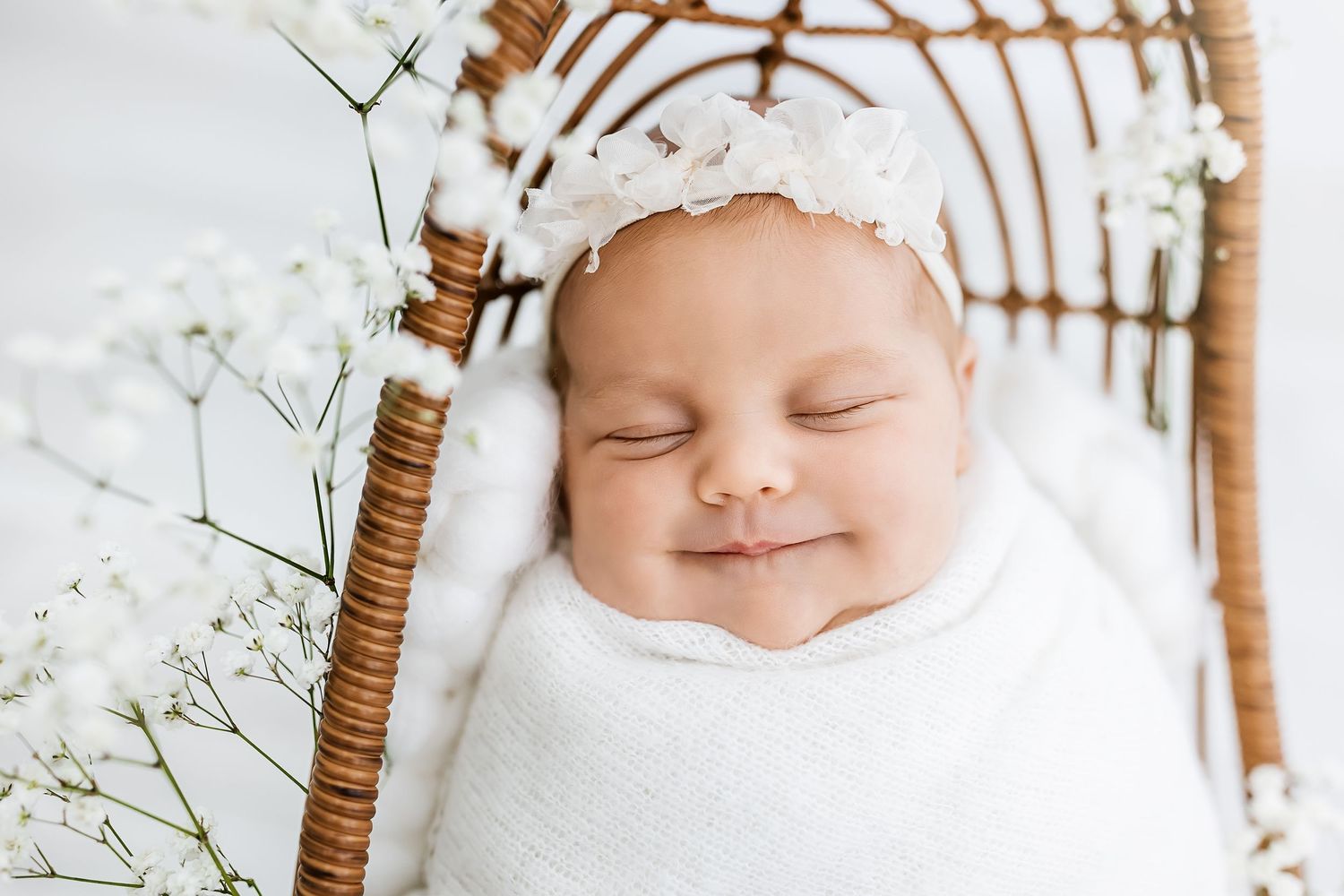 Sweet sleeping baby wearing white knit hat surrounded by delicate baby's breath flowers.