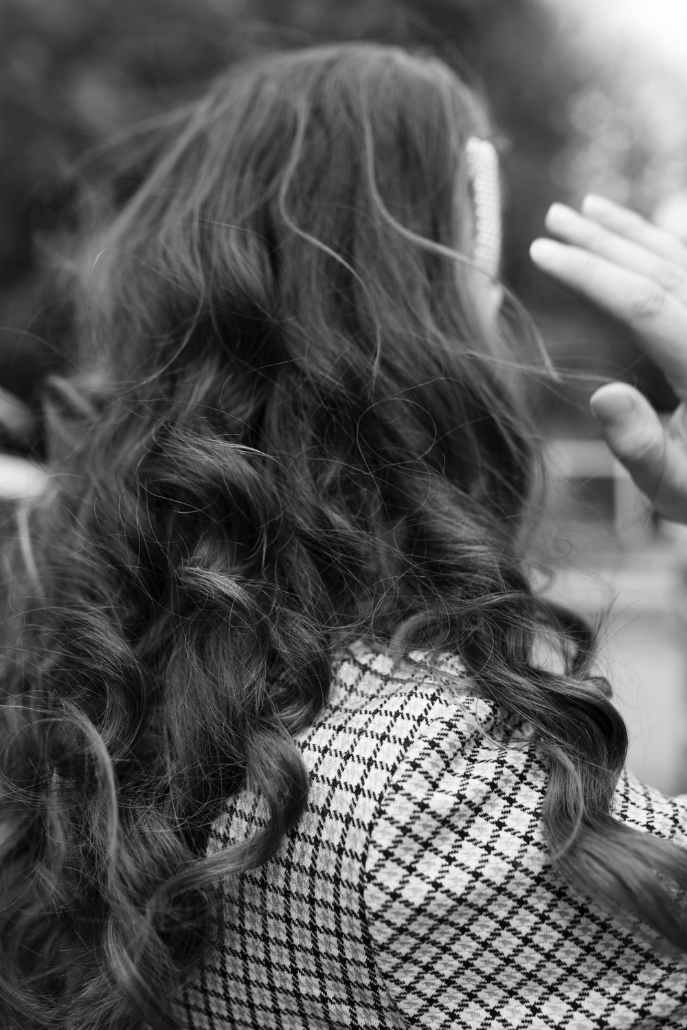 Close-up black and white photo showing long dark curly hair and a patterned garment.