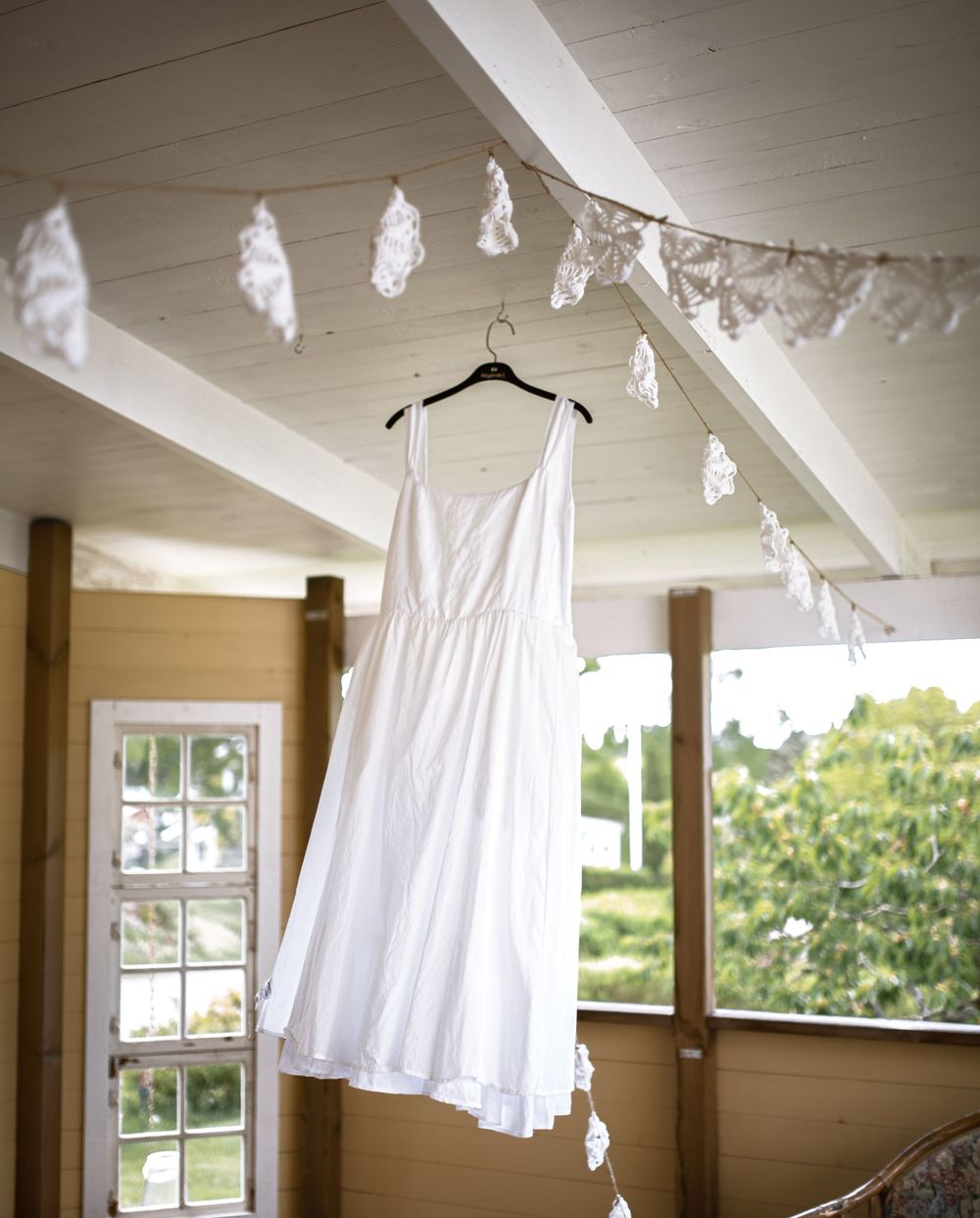 A white wedding dress hangs from a ceiling with delicate white decorations.