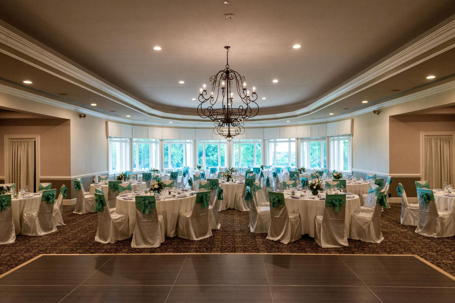 Elegant ballroom with tray ceiling and white-draped chairs set up for a wedding ceremony.