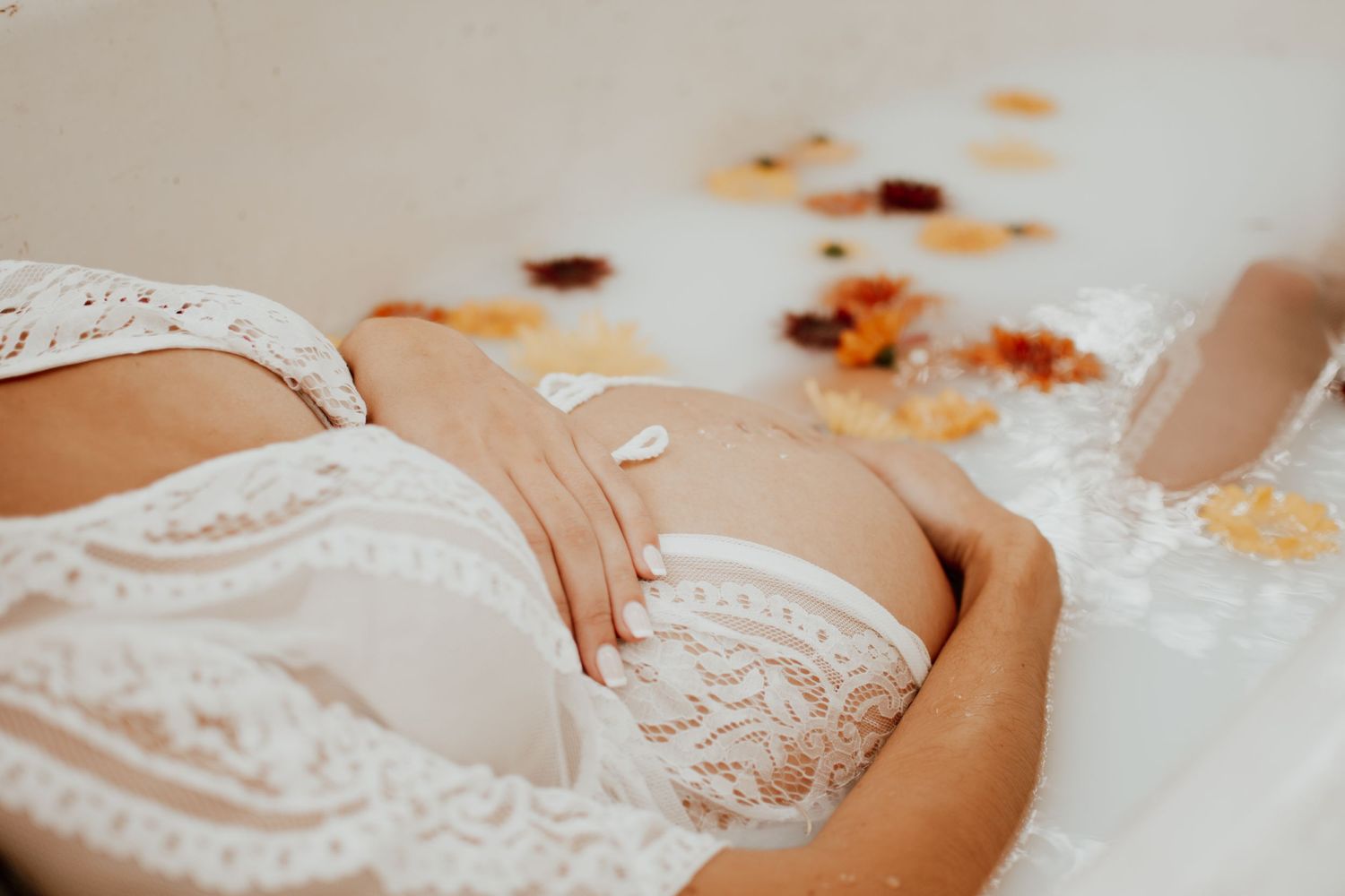 Close up details of a milk bath maternity session with scattered autumn flowers and delicate lace.