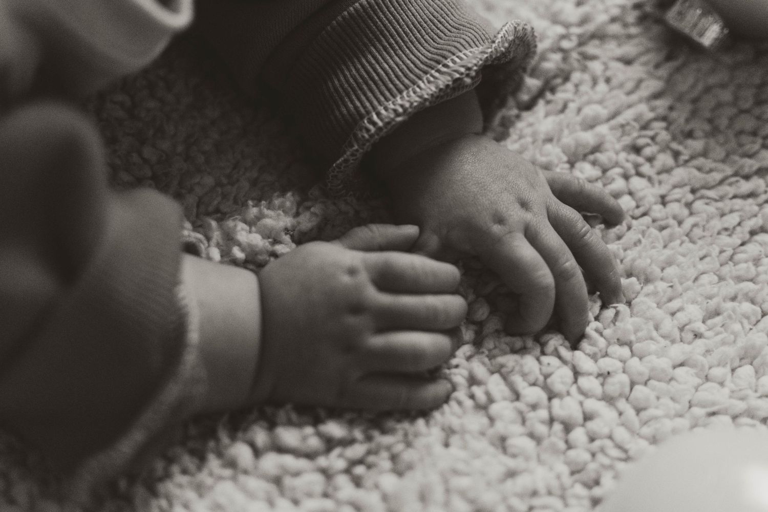 Close up black and white photo of small hands touching a textured carpet.