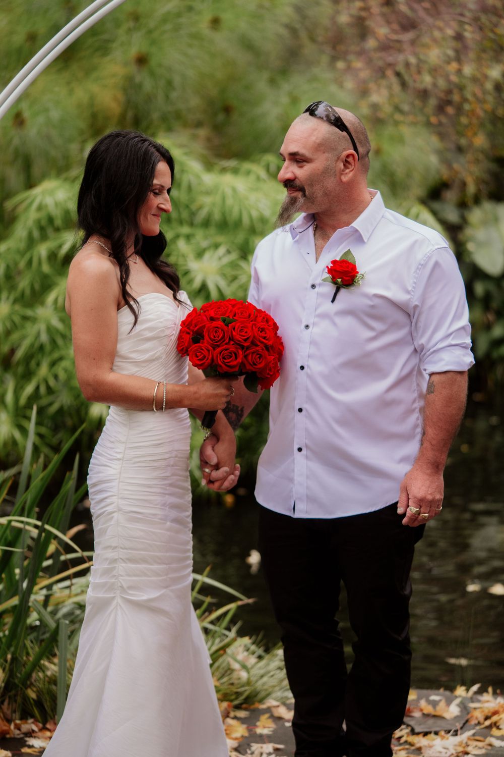 Couple sharing a moment while holding red roses in a garden setting.