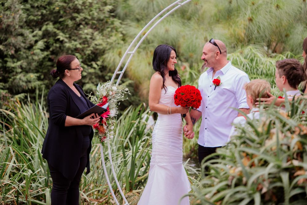 Outdoor wedding ceremony under an arch surrounded by lush greenery.
