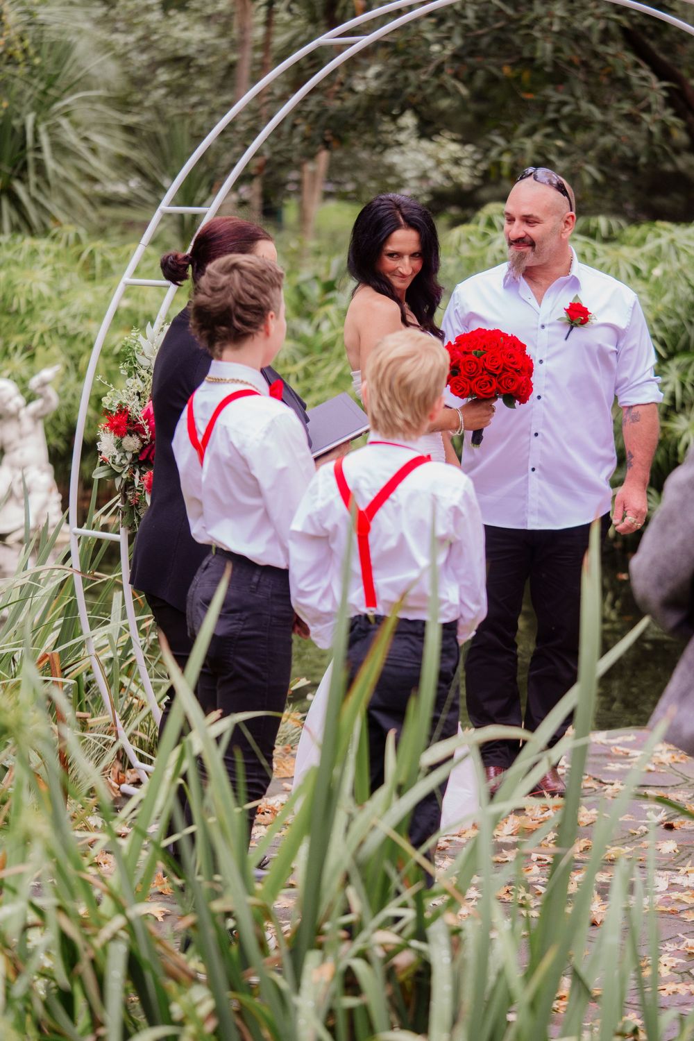 Outdoor photoshoot showing guests gathered in front of lush greenery wearing white and red attire.