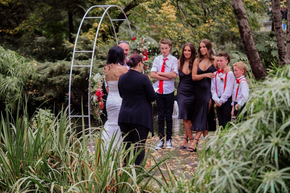 Wedding guests stand together in a garden setting with white shirts and red accents.