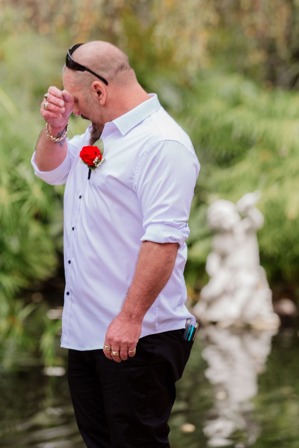 Person wearing white dress shirt and black pants standing by garden pond.