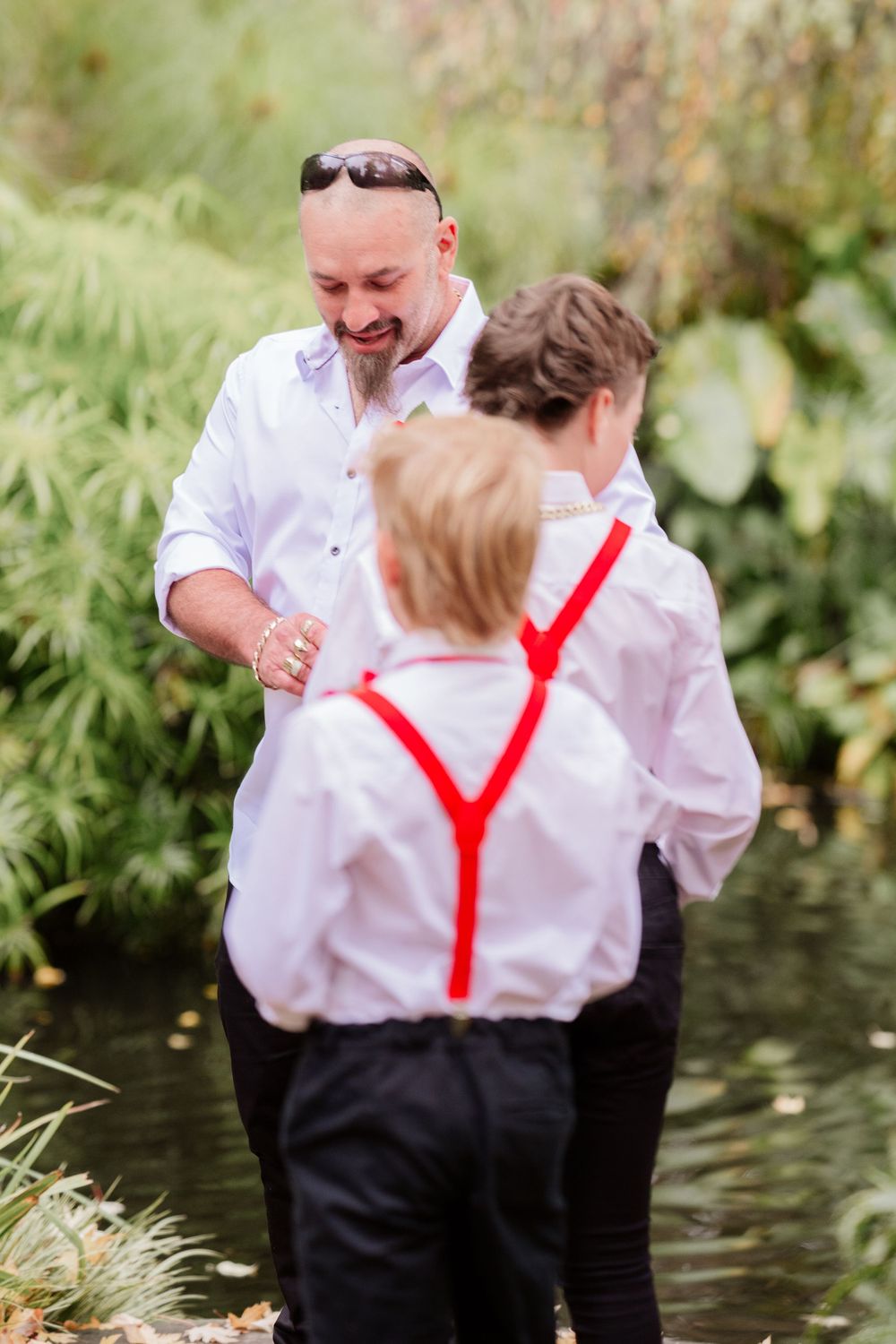 People in coordinated white attire with red suspenders interacting in garden setting.