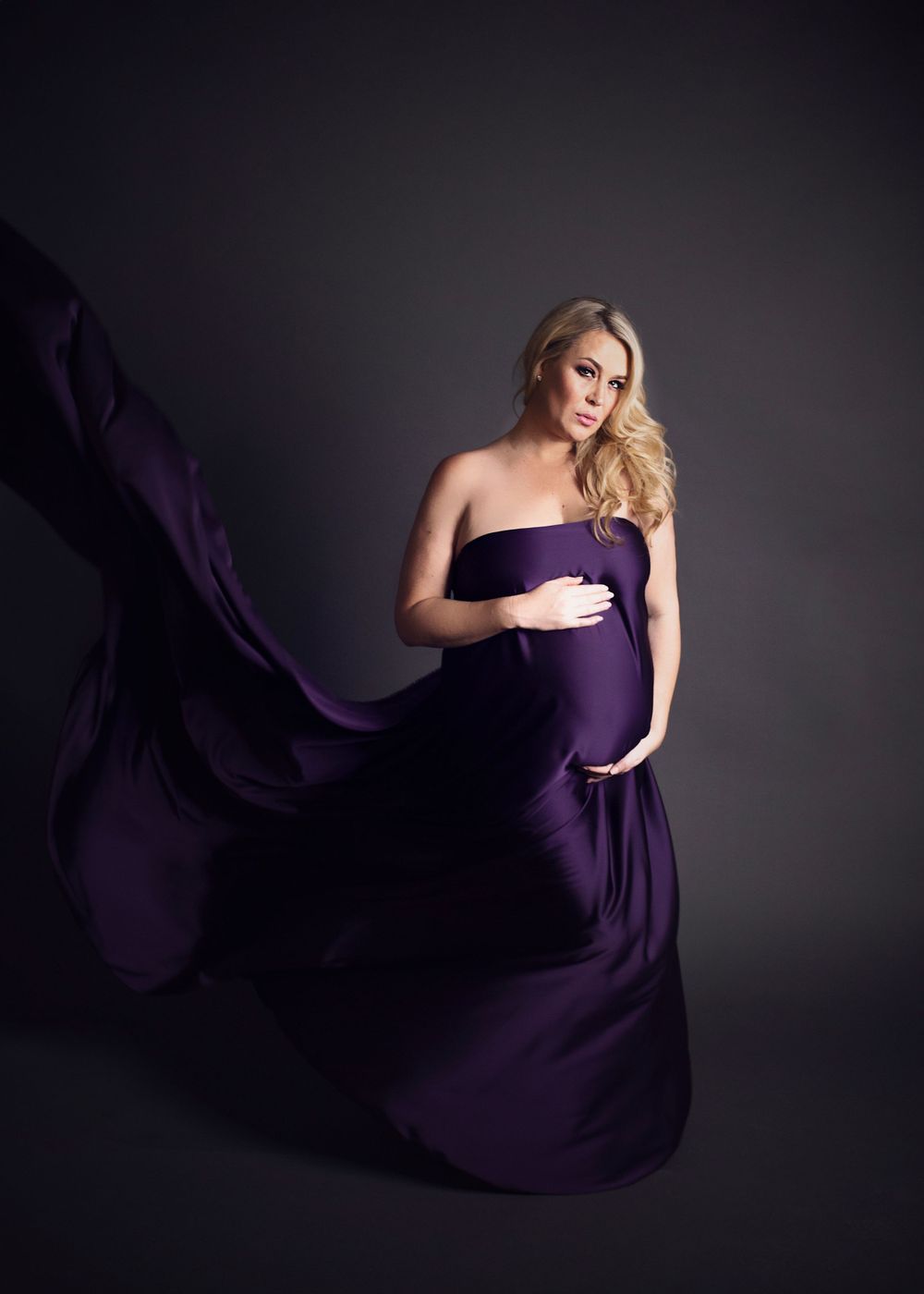 Lady in purple dress posing in studio maternity photo shoot.