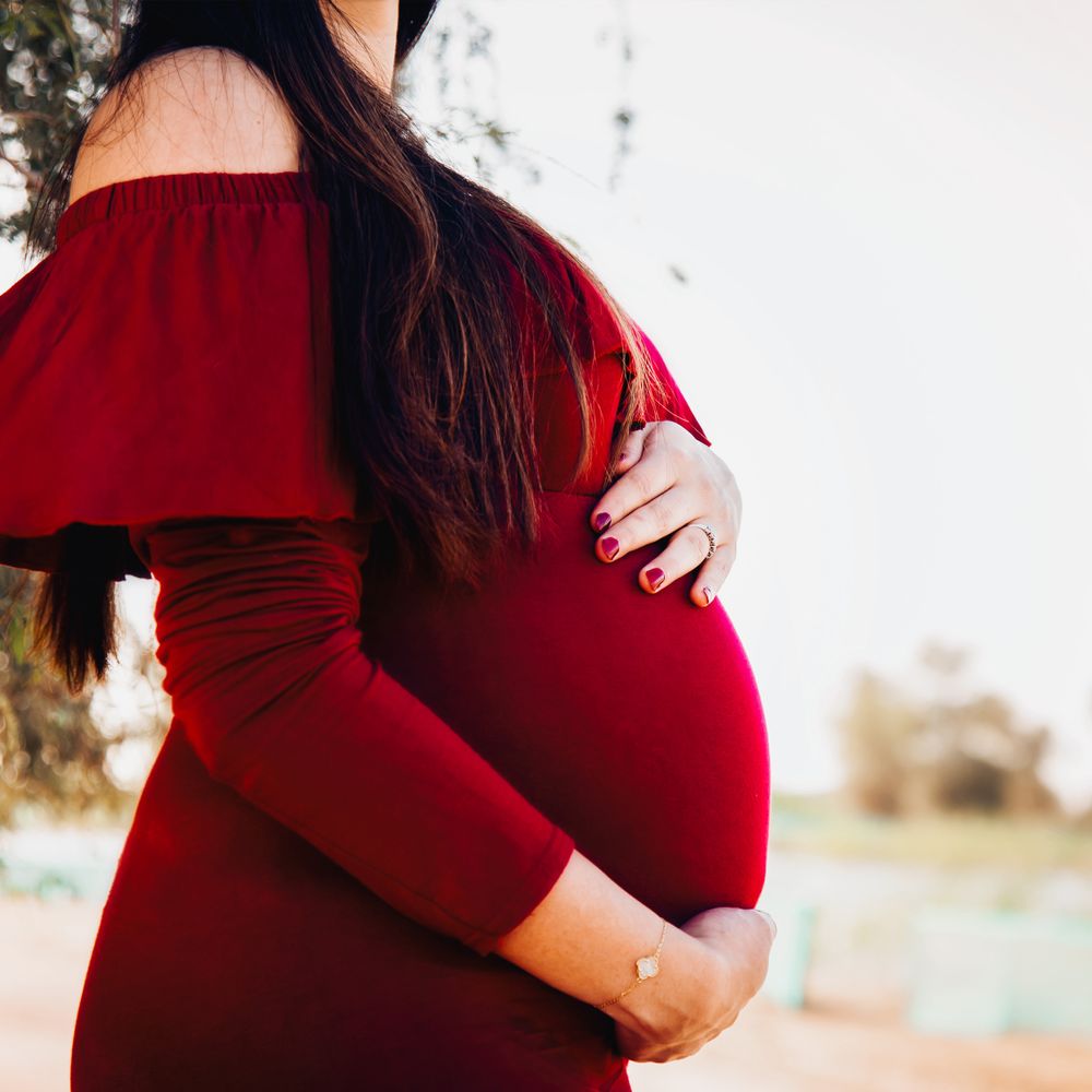 Close up image of a pregnant lady posing in a deep red dress at a lake side.