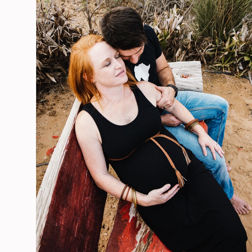Couple having a loving moment on a bench during a maternity photo shoot.