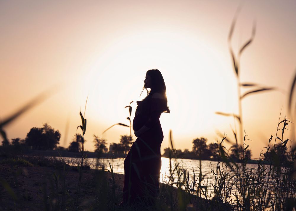 Pregnant woman silhouetted against golden hour at a beautiful lake setting.