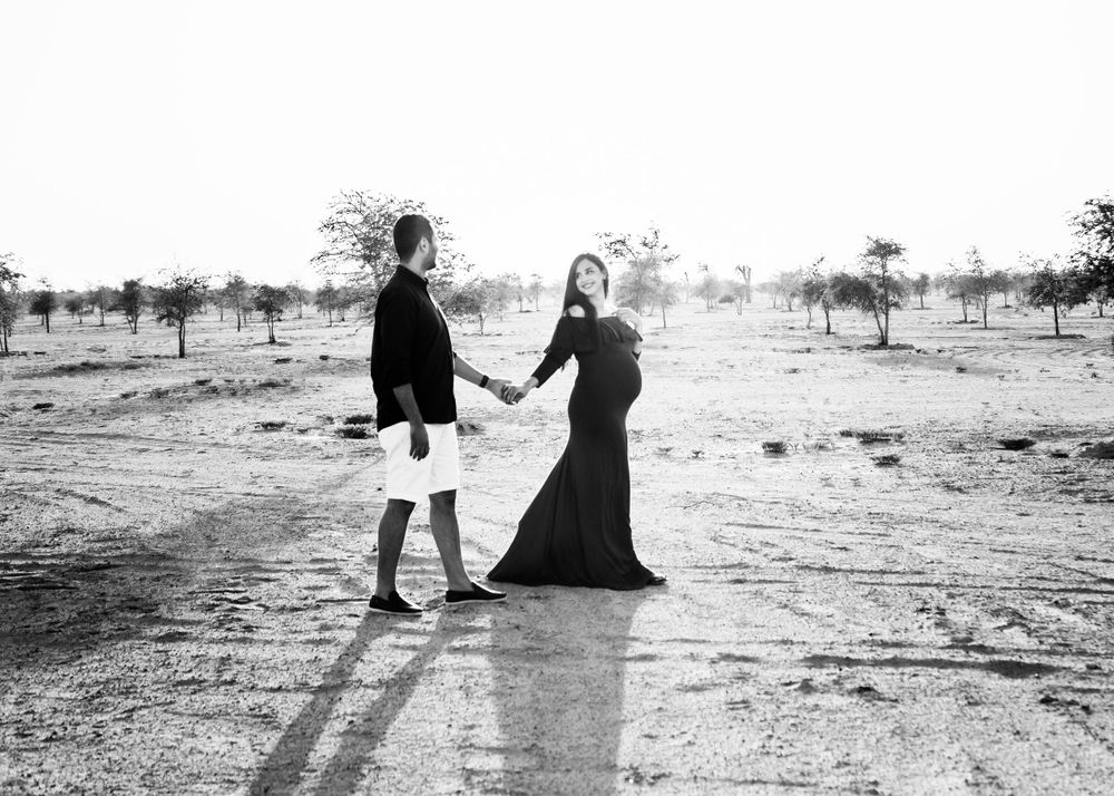Black and white image of a couple walking and holding hands during a outdoor maternity photo shoot.