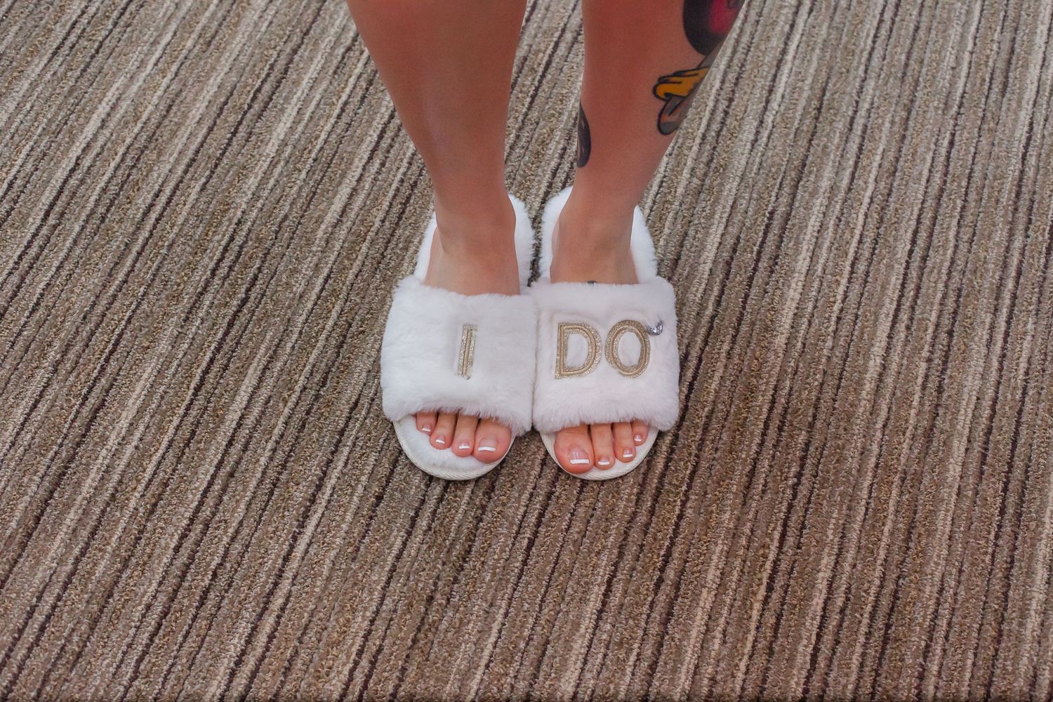 Wedding shoes with 'I DO' text visible on soles against textured grey carpet.