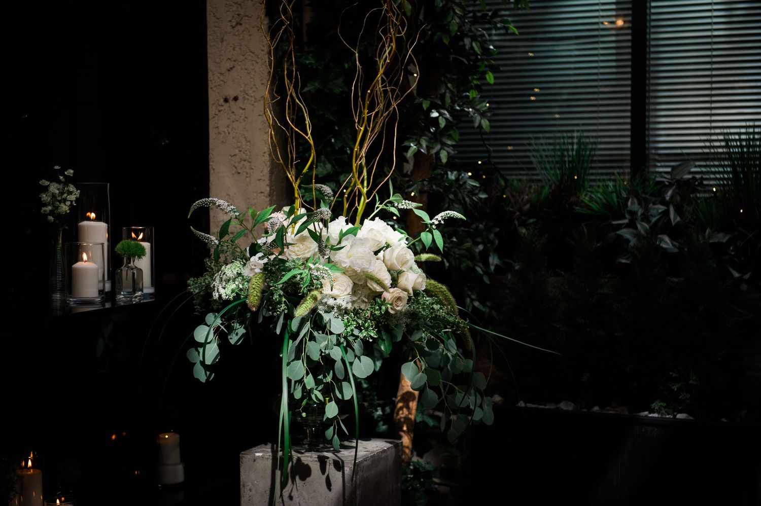Dramatic floral arrangement with white blooms and greenery against dark backdrop.