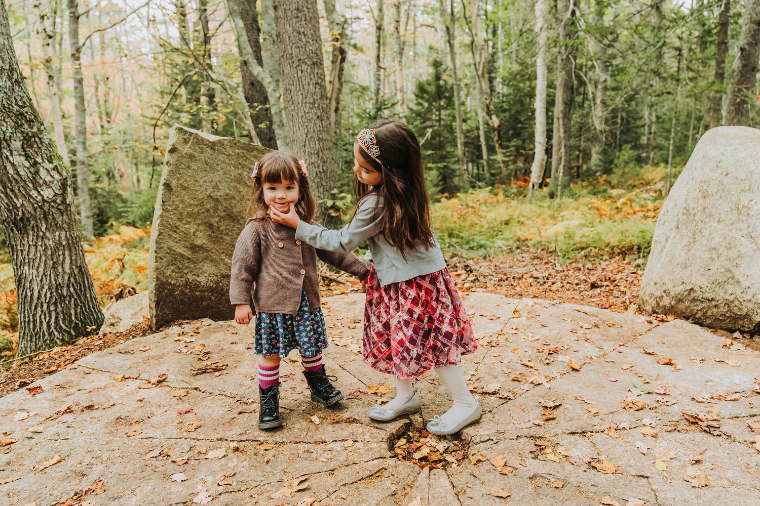 An older sister tries to get her little sister to smile during a family photo session at the Maine Botanical Gardens.
