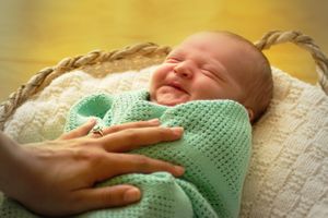 newborn photo baby boy in greem blanket and mums hand and ring claming baby smiling