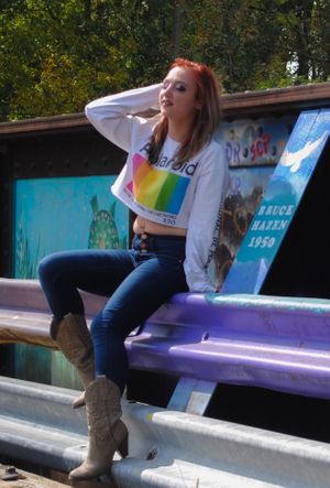 Person in white sweatshirt with rainbow design sits casually on bleachers wearing boots.