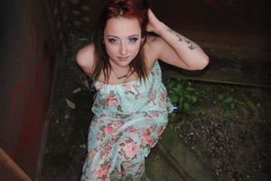 Person in floral dress poses against dark textured background in artistic photoshoot.