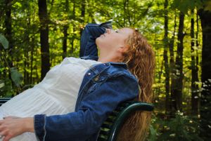 Person in denim jacket leaning back in contemplation surrounded by green forest.