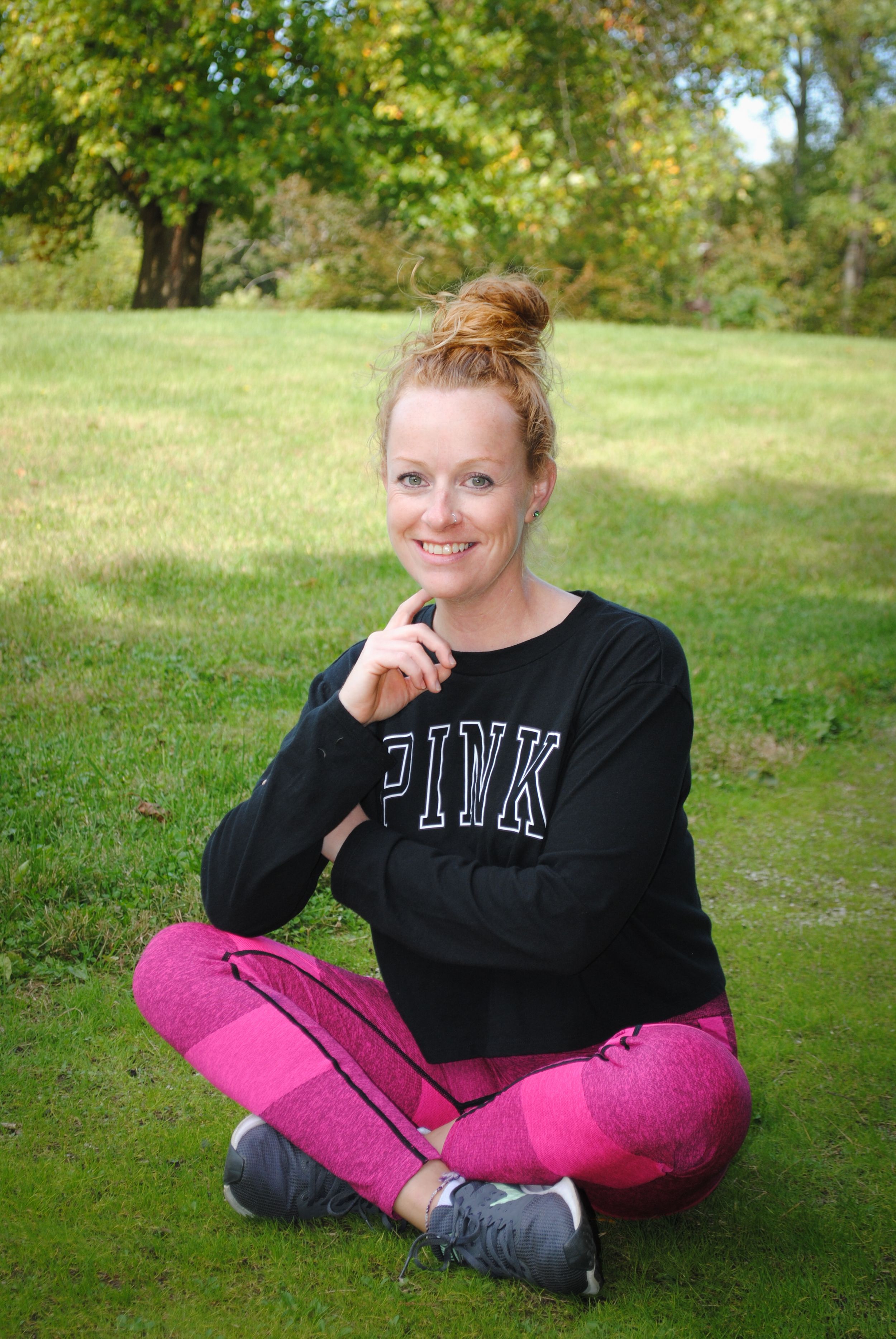 Woman in PINK sweatshirt and pink pants sitting cross-legged on grass outdoors.