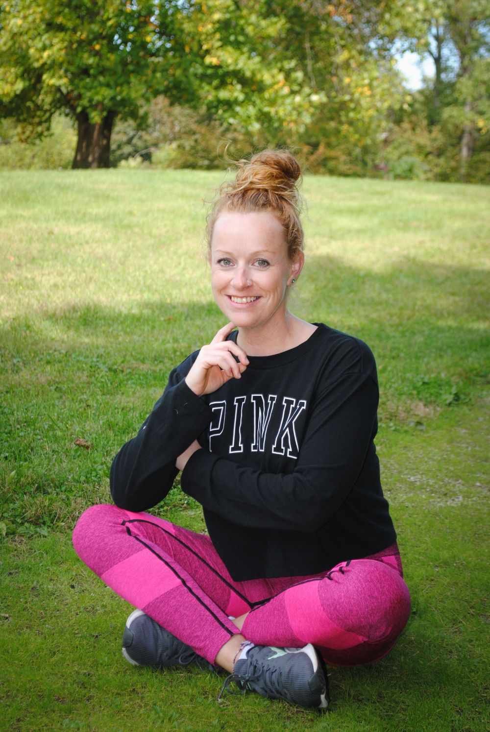 Woman in PINK sweatshirt and pink pants sitting cross-legged on grass outdoors.
