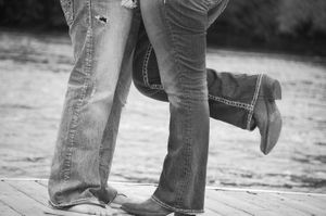 A black and white photo showing two pairs of feet in jeans and boots standing close together.